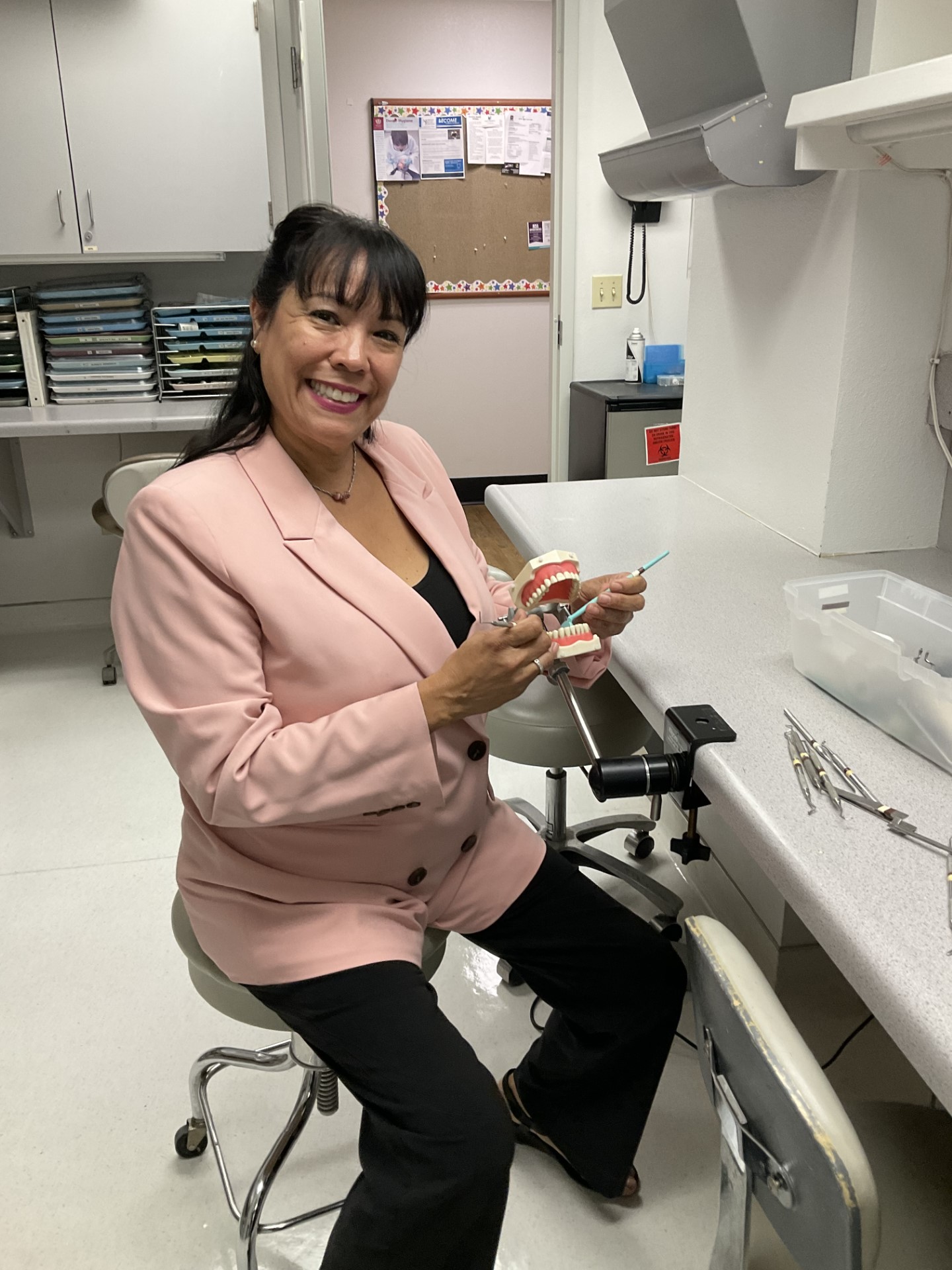 Woman holding model of teeth showing cleaning technique in dental office 