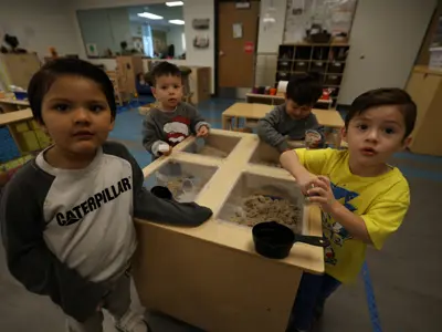 Four young boys looking up from sandbox in classroom